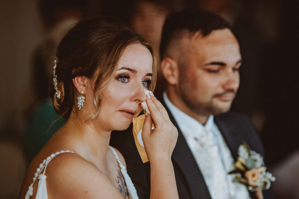 Emotionale Braut wischt Tränen während Hochzeit neben Bräutigam weg Titel: Emotionale-Hochzeit-Momente.